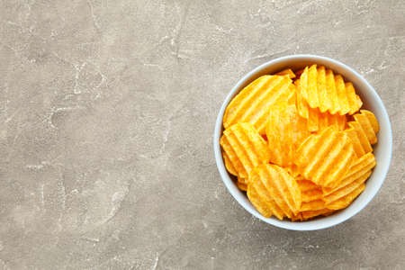 Potato chips in blue bowl on gray concrete background. Top view
