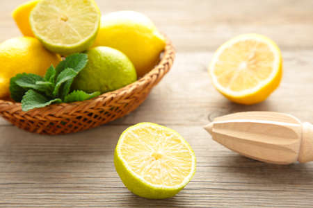 Fresh lime and lemon in basket with citrus juicer stick on gray wooden background. Top viewの写真素材