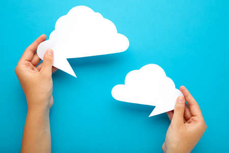 Two hands holding up speech bubbles on blue. Top view