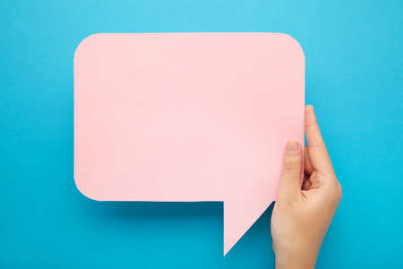 Hand holding an pink speech bubble on blue background. Top viewの写真素材