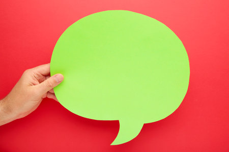 Hand holding an empty speech bubble on red background. Top view