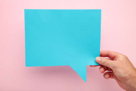 Hand holding an blue speech bubble on pink background. Top viewの写真素材