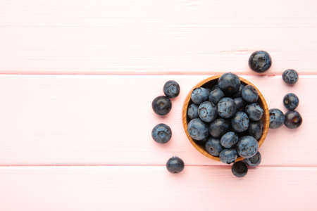 Fresh blueberries in small wooden bowl on pink background. Top viewの写真素材