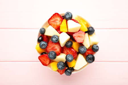 Salad with fresh fruits and berries on pink wooden background with copy space. Top viewの写真素材