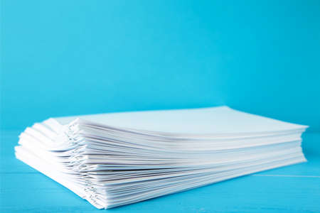 Colorful paper clip with pile of overload white paperwork on blue. Top viewの写真素材