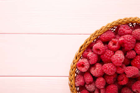 Fresh raspberry in a basket on pink wooden background. Top view