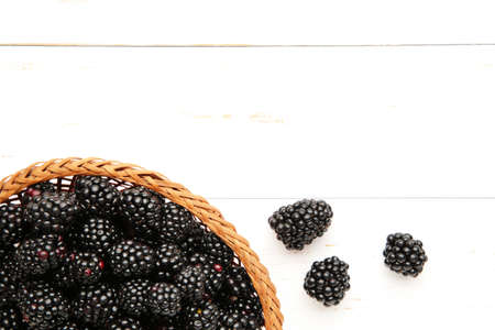 Blackberry in a wicker basket on a white wooden background. Top view