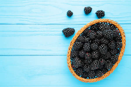 Blackberry in a wicker basket on a blue wooden background. Top viewの写真素材