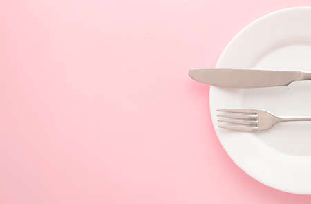 White empty plate with fork and knife on a pink table. Top viewの写真素材