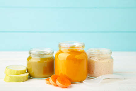 Glass jars with nutrient baby food on blue background. Vegetable puree with spoon.の写真素材