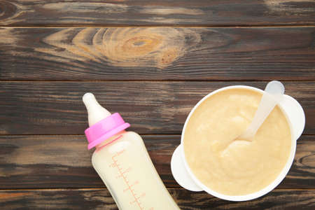 Milk and bowl with porridge for baby on brown background. Vertical fotoの写真素材