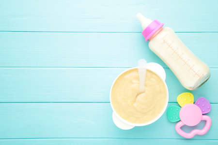 Milk and bowl with porridge for baby on blue background. Baby foodの写真素材