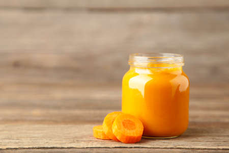 Jar of baby puree with carrot on gray wooden background. Vegetable puree. Top viewの写真素材