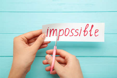 man hand holding card with the text impossible, cutting the word im so it written possible. success...