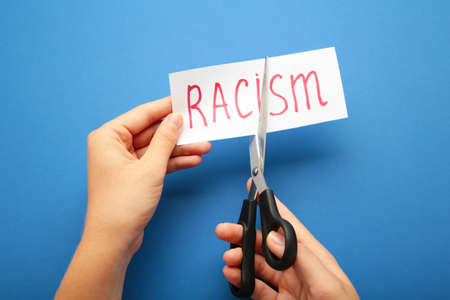 Hand holding card with the text racism. Top view of black scissors and cutted paper card with word...