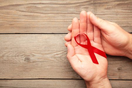 A female hands holding an aids red ribbon on gray. Top view