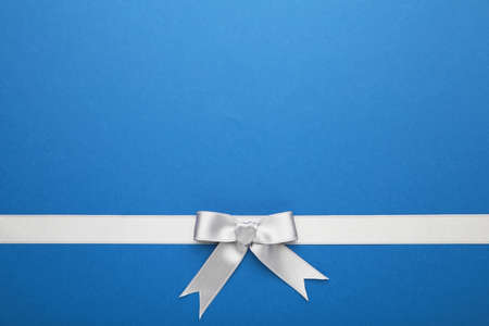 Silver ribbon and bow on blue pastel background. Top view.の写真素材