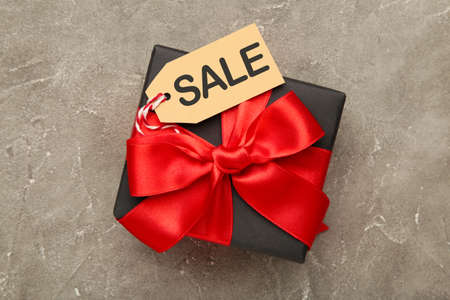 Sale price tag on black gift on gray concrete background. Black Friday sales discount composition. Top view.の写真素材