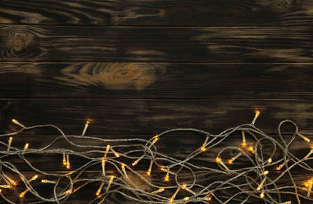 Glowing Christmas tree garland in the form of a frame on a brown wooden background. Top view.