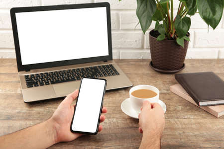 Close up male hands holding big smart phone, businessman using technology sitting at wooden desk....