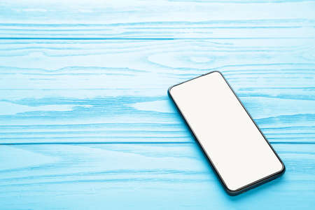 Black mobile smartphone with blank screen on blue background. Top view.