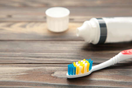 Toothbrushes in glass with tube of toothpaste on brown background. Top view
