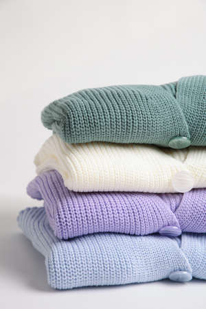 Stack of cozy knitted sweaters on light background. Top view