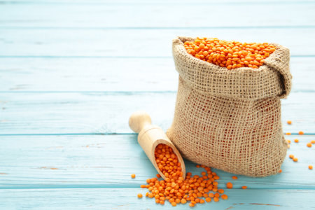 Red lentils in a wooden spoon and bag on blue wooden background. Close up.