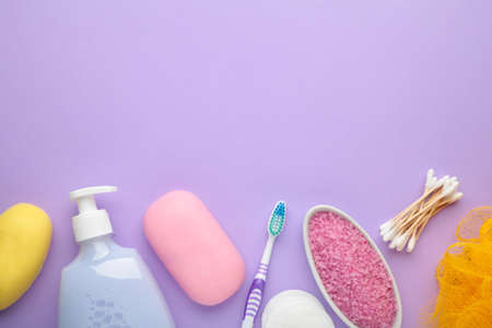 Bottle of pink shower gel, soap, bath salt and toothbrush on purple background. Top view