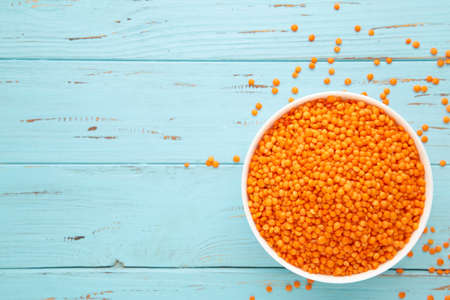 Red lentils in bowl on a blue wooden table. Top view.