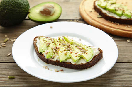 Avocado sandwich on dark rye bread made with fresh sliced avocados on brown background. Top view