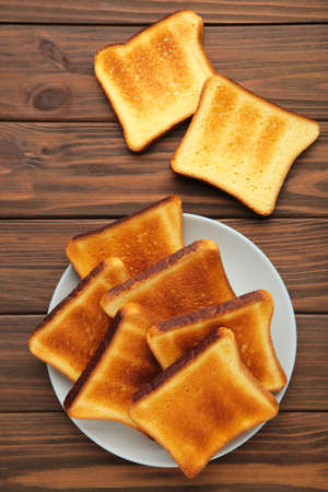 Pile of toasted bread slices on gray plate on brown background. Top view