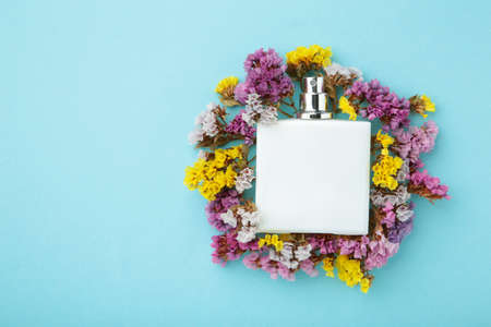 Bottle of perfume with flowers on blue background. Top view