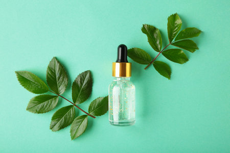 Natural skincare bottle container and organic green leaf, flowers ingredients with the laboratory glassware on mint background. Essential oil. Top viewの写真素材