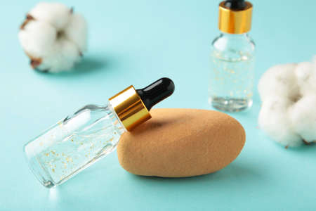 Serum or oil bottle with pipette and cotton twig on blue background. Beauty product, skin care concept. Vertical photoの写真素材