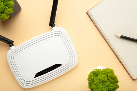 Wireless WiFi router on beige background with notebook on beige. Top view