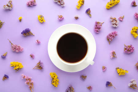Cup of coffee with flowers on purple background. Flat lay, top viewの写真素材