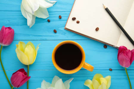 Notebook with cup of coffee and tulips on blue background. Top view
