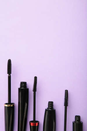 Black mascara wand and tube on purple background with copy space. Vertical photo. Top viewの写真素材