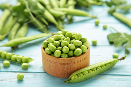 Green peas in wooden bowl on blue wooden background. Top viewの写真素材
