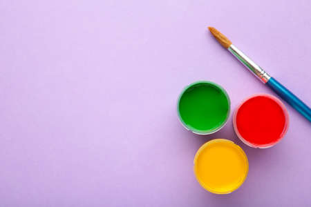 Multicolored jars of gouache and a brush on a purple background. Top view.の写真素材