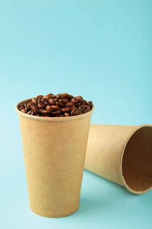Coffee beans and paper coffee cup on blue background. Top view.