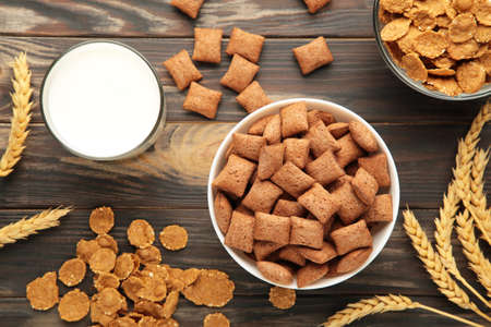 Variety of cereals in blue bowls, quick breakfast and milk on brown wooden background. Top view