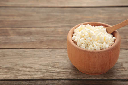 Cottage cheese for breakfast in wooden bowl on brown background. Top view