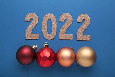 Inscription 2022 with red christmas balls on blue background. Top view