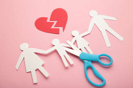 Scissors cutting paper cut of family on pink background. Broken family concept, divorce. Top view