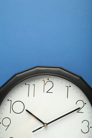 Black wall clock isolated on blue background. Top view.