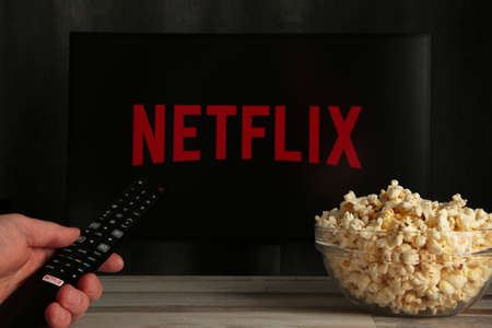 Nikolaev, Ukraine - November 20, 2021. Man with TV remote control in hand and Netflix logo in...