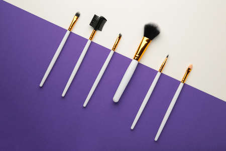 Various makeup brushes on purple and gray background with copy space. Top view
