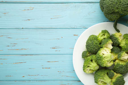 Bunch of fresh green broccoli on white bowl on blue wooden background. Top view.の写真素材